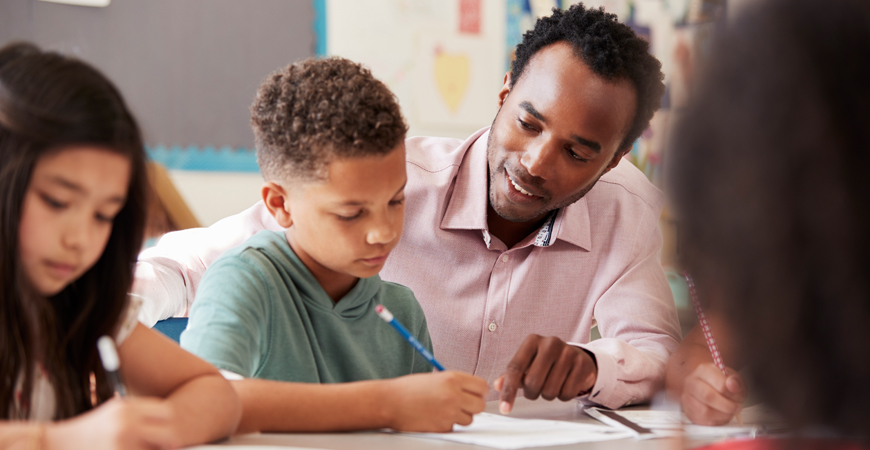 Teacher Preparation Program - mature teacher working with student at desk.